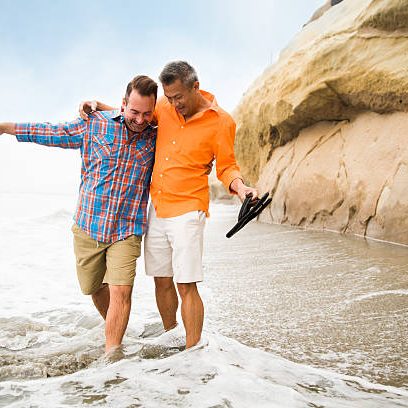 Affectionate interracial gay couple at a beach getting splashed by an unexpected wave.